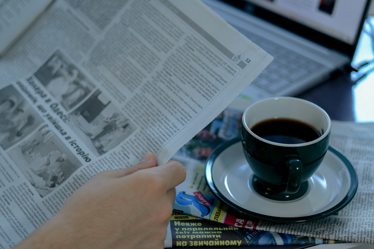 Mano che tiene un giornale accanto a caffè e laptop.